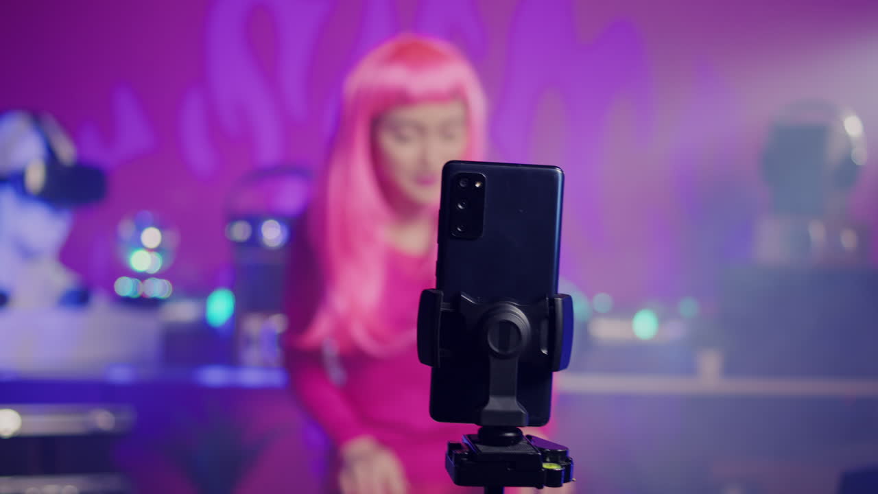Una donna con i capelli rosa sta usando uno smartphone su un treppiede per registrare un video