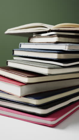 vertical video of open book on stack of books on green background, in slow motion