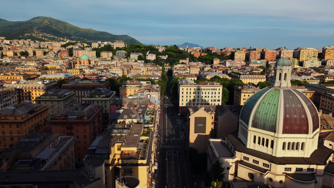 Drone advancing through Genoa, brushing past a tall modern building with city reflections, passing close to a large dome and revealing a street below