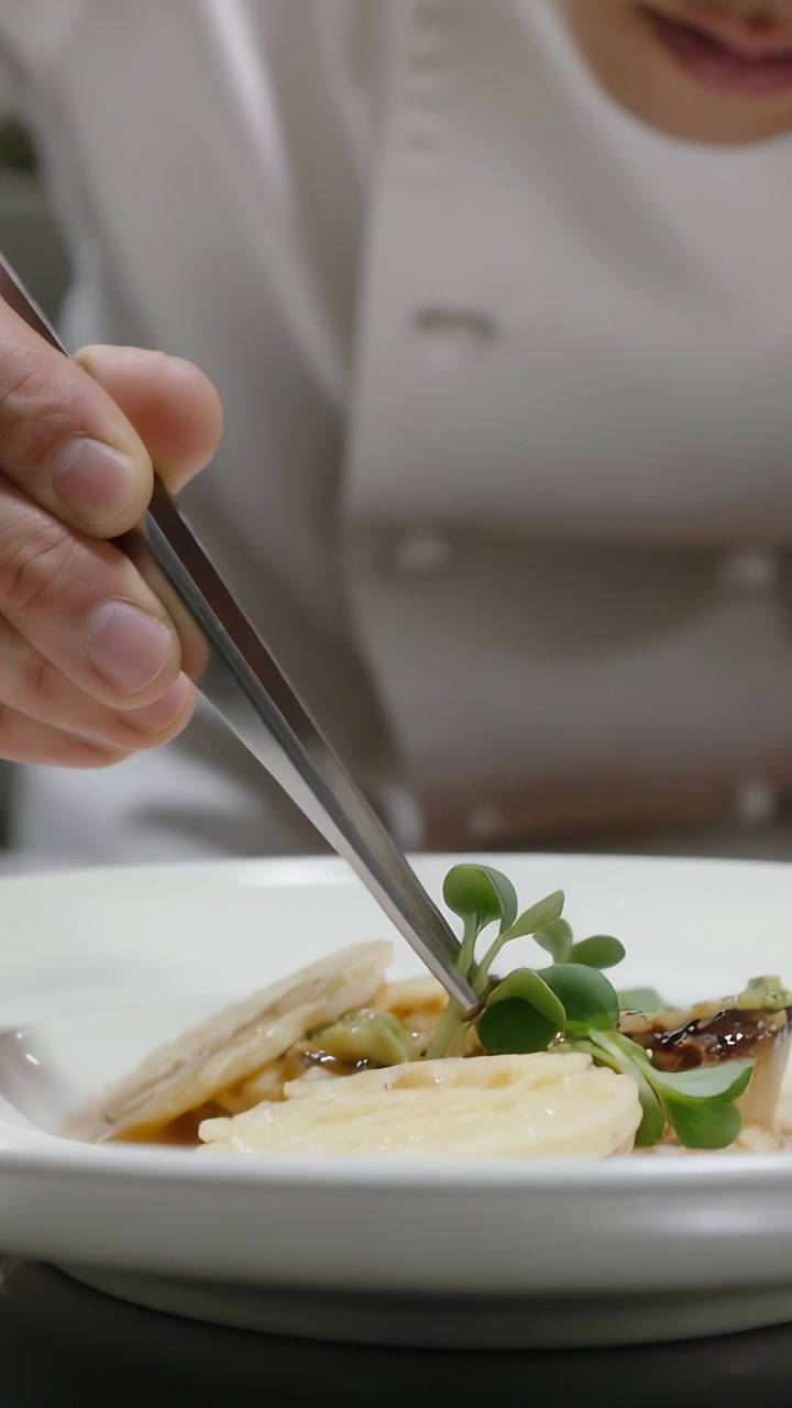 Vertical video: Lifting tweezers, chef in coat placing microgreens on plate for service in kitchen