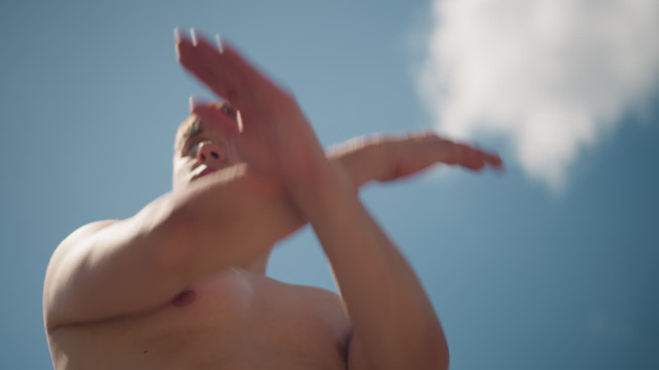 맑은 햇살 아래 평화롭게 스트레칭하는 남자, 상의를 탈의한 남자가 밝은 하늘 아래서 워밍업 중에 고요한 야외 스트레칭을 하고 있어요.