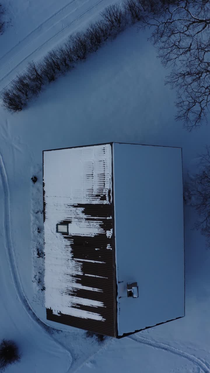 Vertical aerial top down drone view of a single family home roof covered in snow on a winter day. From sunny to cloudy weather.