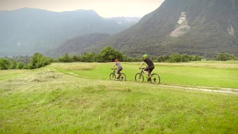 aerial view of a couple driving mountain bikes on dirt road surrounded by hills.