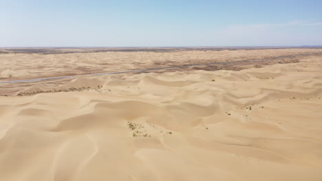 panning drone footage of a long car road lined with sand dunes in the gobi desert