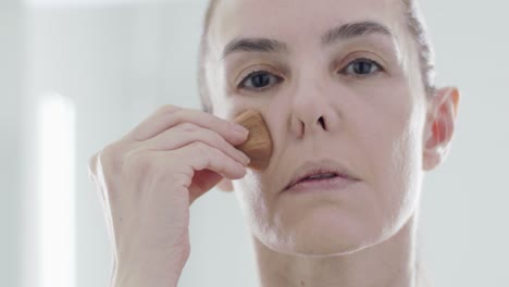 caucasian woman 40s using brush to put on foundation on her face for facial care and anti-wrinkle