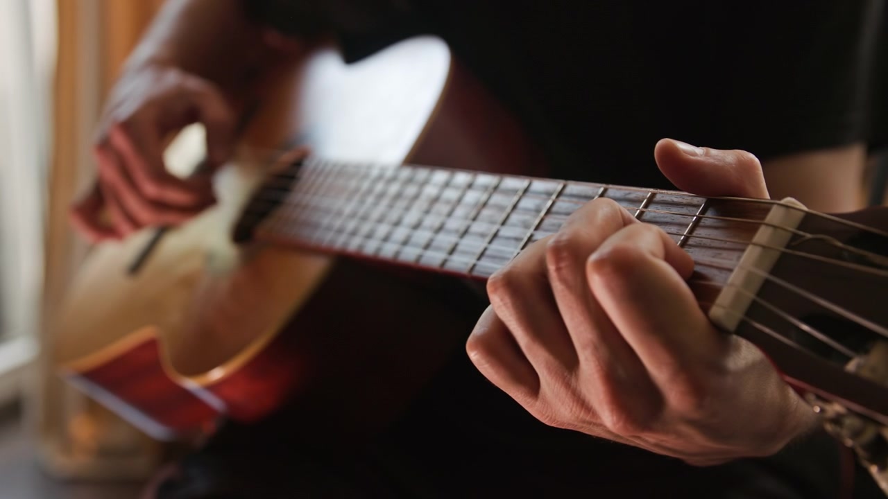 Un primo piano di una persona che suona una chitarra classica acustica al rallentatore, pizzicando gli accordi con le dita. Il video presenta una splendida illuminazione realistica e calda e un'ottima qualità estetica visiva
