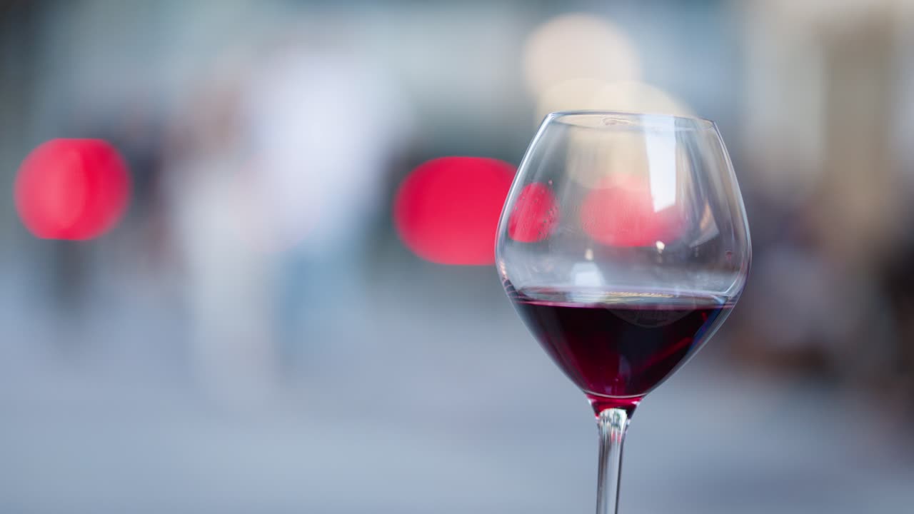 Hand pours red wine into glass with bokeh lights, elegant outdoor evening setting, shallow focus