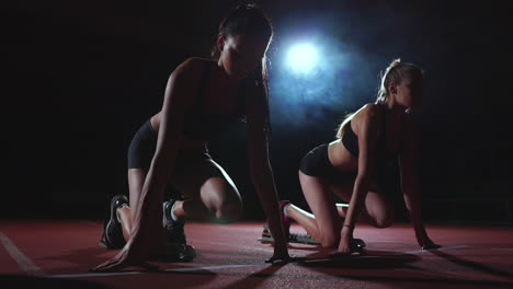 tres chicas con ropa negra están en las plataformas de salida para comenzar la carrera en la competencia a la luz de las luces y correr hacia la meta