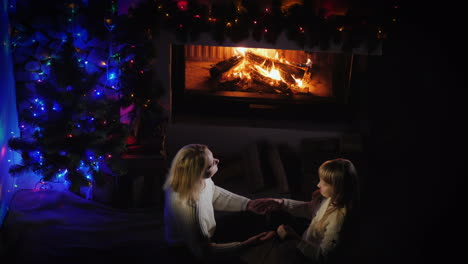 mom plays with her daughter near the fireplace and christmas tree a good time together