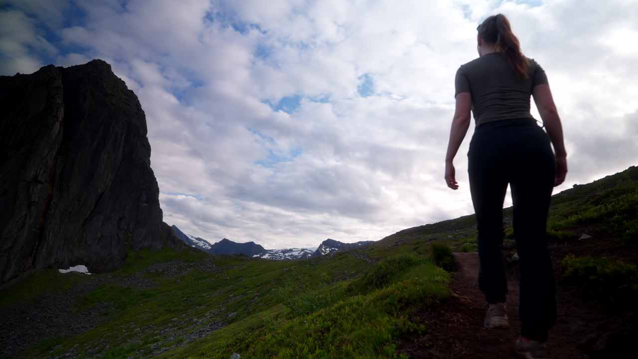 Female hiker traverse dirt trail on scenic hike up to Segla mountain, Fjordgard