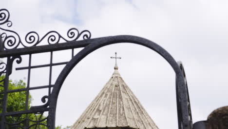 Focusing-on-cross-on-church-tower-top-through-iron-gate-doorway-arch