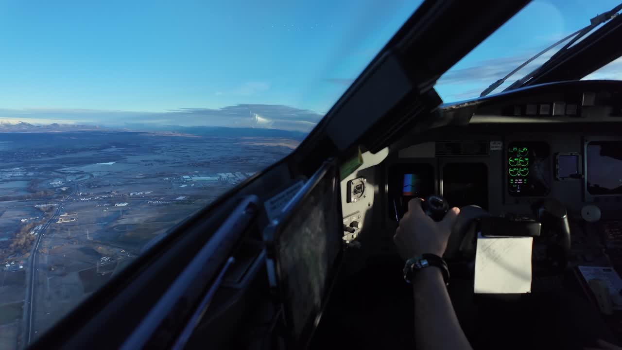 Sudut pandang pilot saat terbang di atas lanskap beku di waktu senja kebiruan, dengan pemandangan tangan pilot yang mengendalikan pesawat secara manual menggenggam tuas kemudi.