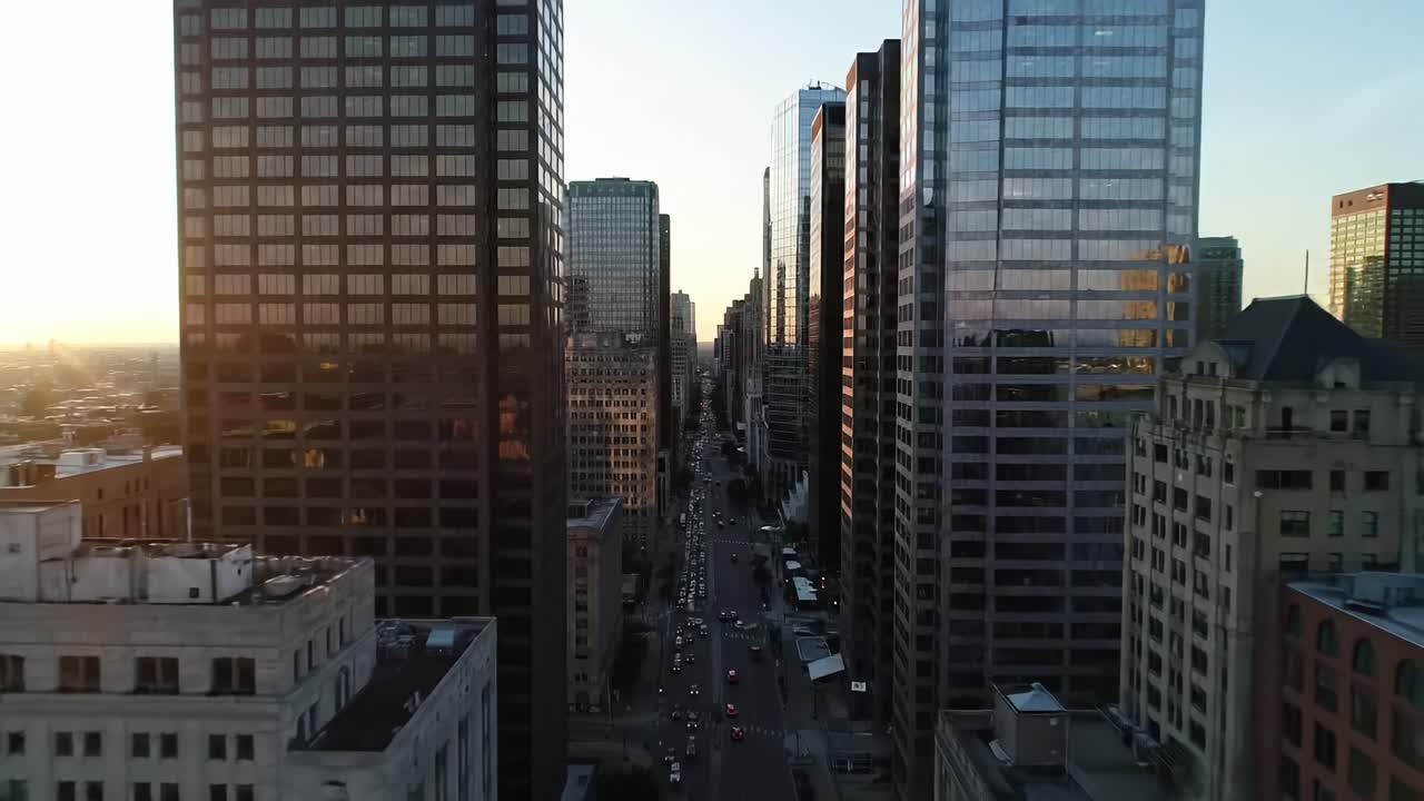 Cityscape at sunset showcases tall glass structures and busy streets filled with cars. Golden light reflects off buildings as the sun sets, creating a vibrant urban scene.