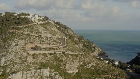 Aerial-shot-of-winding-hillside-roads-and-houses-by-a-beautiful-azure-Mediterranean-bay-in-Spain-around-sunset-on-a-sunny-day