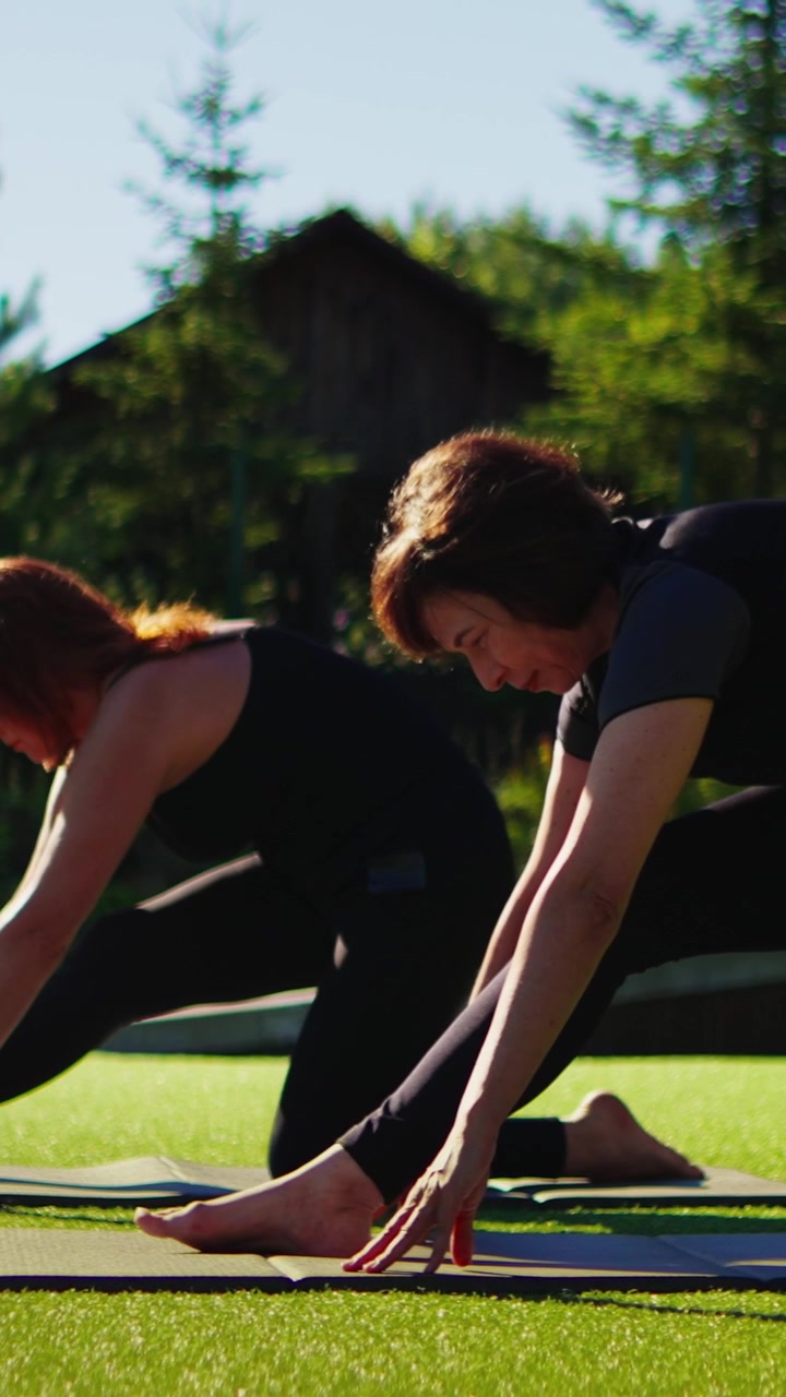 Zwei Frauen praktizieren Yoga im Freien auf grünem Gras