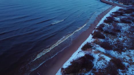 Drone-flight-revealing-cold-winter-beach-with-snow-in-blue-hour