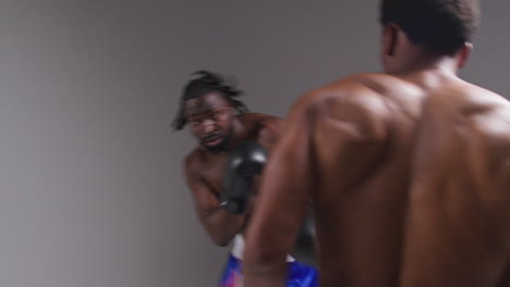 real time action studio shot of two male boxers wearing gloves fighting in boxing match against grey background