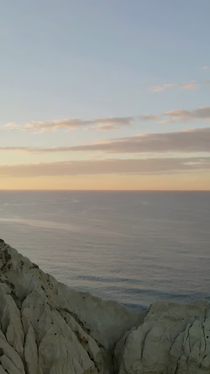 Video verticale: Telecamera in movimento che rivela l'oceano da una scogliera rocciosa all'alba, con nuvole alla deriva.