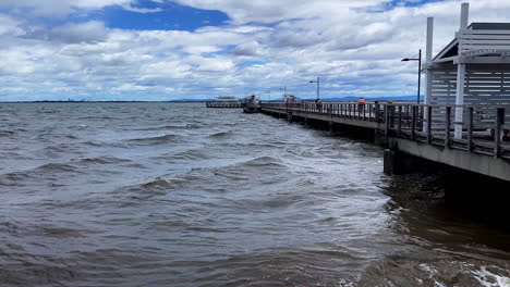 Slow-panning-shot-of-ocean-waves-and-boardwalk-at-Woody-Point-Jetty-on-a-cold-sunny-morning