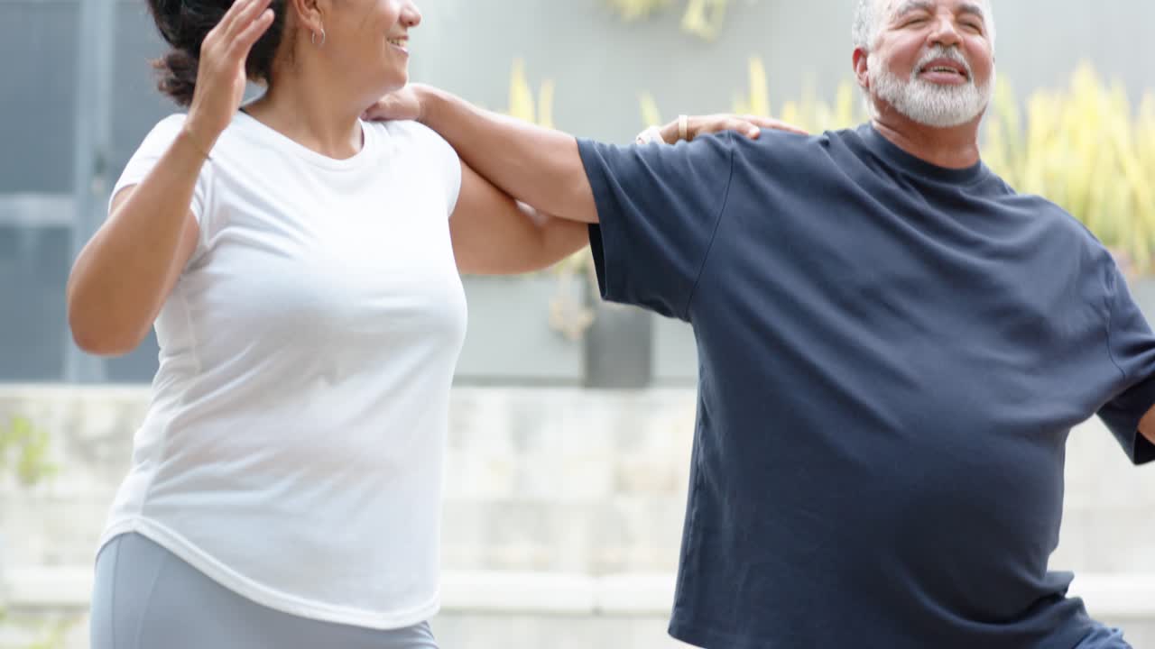 African American couple linking shoulders holding tree pose on patio mats for balance and bottle