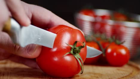 male hand with a knife cut a ripe tomato.