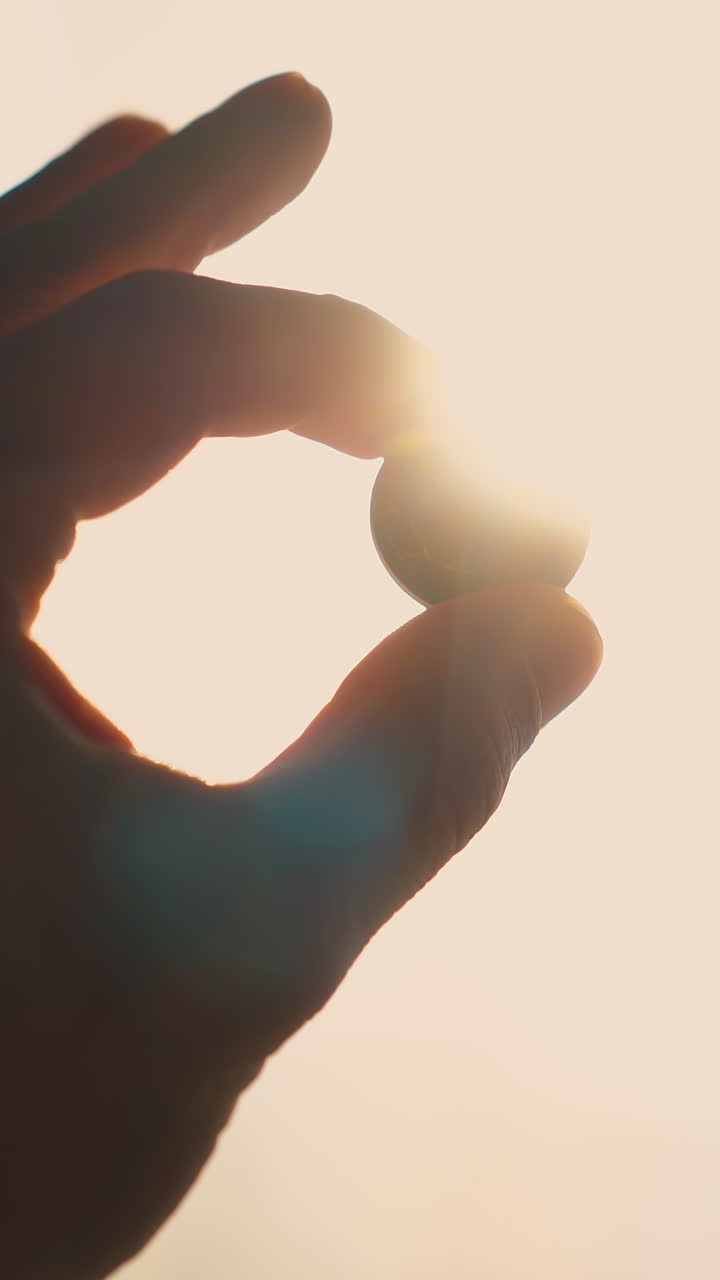 CU: silhouette of elegant man hand with little coin against bright sun backlight near window in dark room extreme closeup