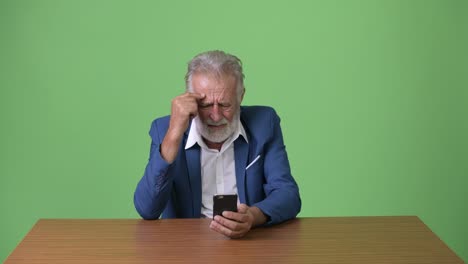 handsome senior bearded businessman against green background