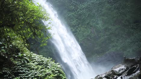 slow motion panning shot in front of a gushing nungnung waterfall in bali, indonesia following a rain storm
