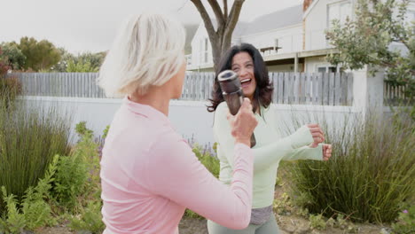 Two-diverse-senior-women-walking-with-water-bottles-talking-on-sunny-day,-slow-motion