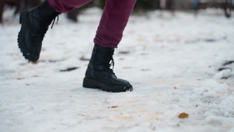 vista lateral de una persona con botas negras saltando en una pierna en un entorno al aire libre cubierto de nieve, el calzado crea pequeñas hendiduras en la nieve