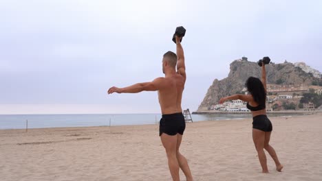 diverse strong sportsman and sportswoman doing exercises with dumbbells on beach at