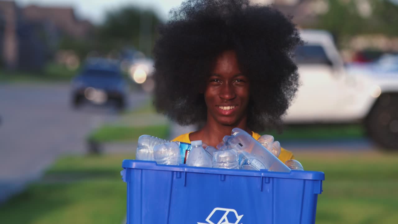 African American adolescents with huge Afro smiling as he hold recycle bin full of plastic bottles