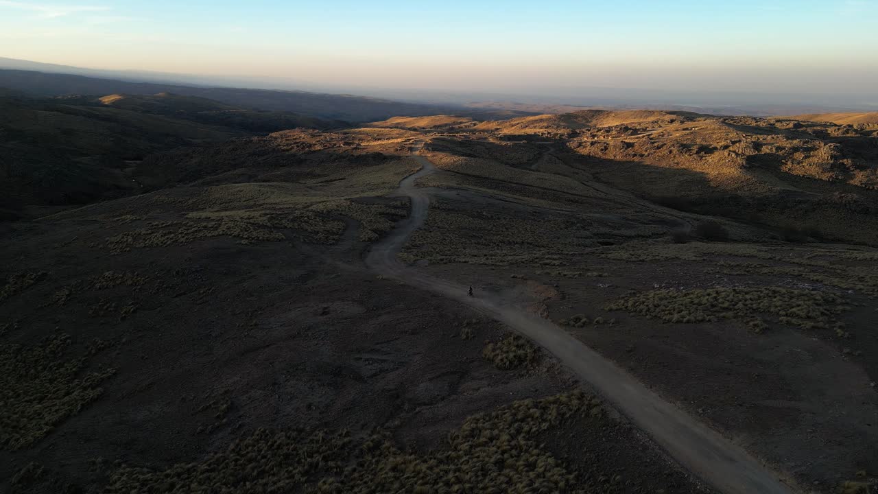 drone aereo di una motocicletta che guida su una strada di montagna accidentata durante il tramonto