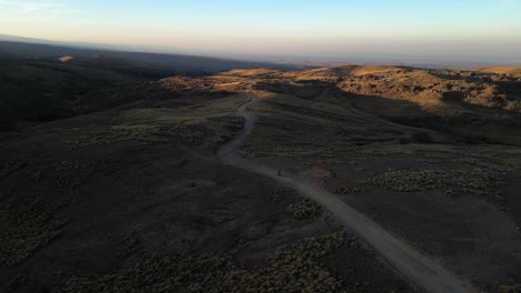 aerial drone shot of a motorcycle driving on a rough mountain road during sunset
