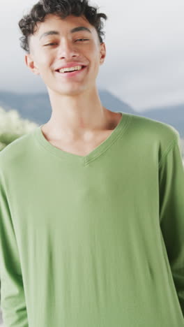 vertical video of portrait of happy biracial teenage boy in long sleeved green t shirt, copy space
