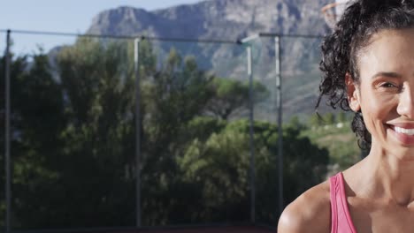 Half-portrait-of-happy-biracial-female-basketball-player-on-sunny-court,-copy-space-in-slow-motion