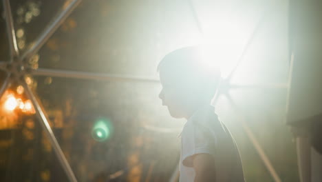 small kid stands against light of lantern behind tent window. tired cute preschooler goes to rest in evening at resort on glamping area slow motion backside view closeup