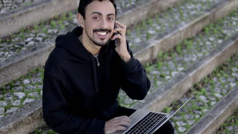 Hombre-Con-Computadora-Portátil-Y-Teléfono-Inteligente-Sonriendo-A-La-Cámara