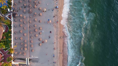 turistas en la playa de los muertos con sombrillas de paja al atardecer en puerto vallarta méxico, antena de arriba hacia abajo