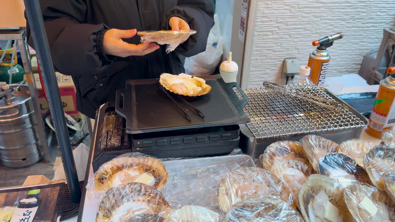 A vendor prepares fresh scallops with butter and soy sauce at a Japanese street market