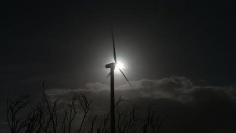 "a stunning night drone shot of a wind turbine gracefully rotating under the stars. its blades, subtly illuminated, cut through the darkness as the structure silently generates clean, renewable energy