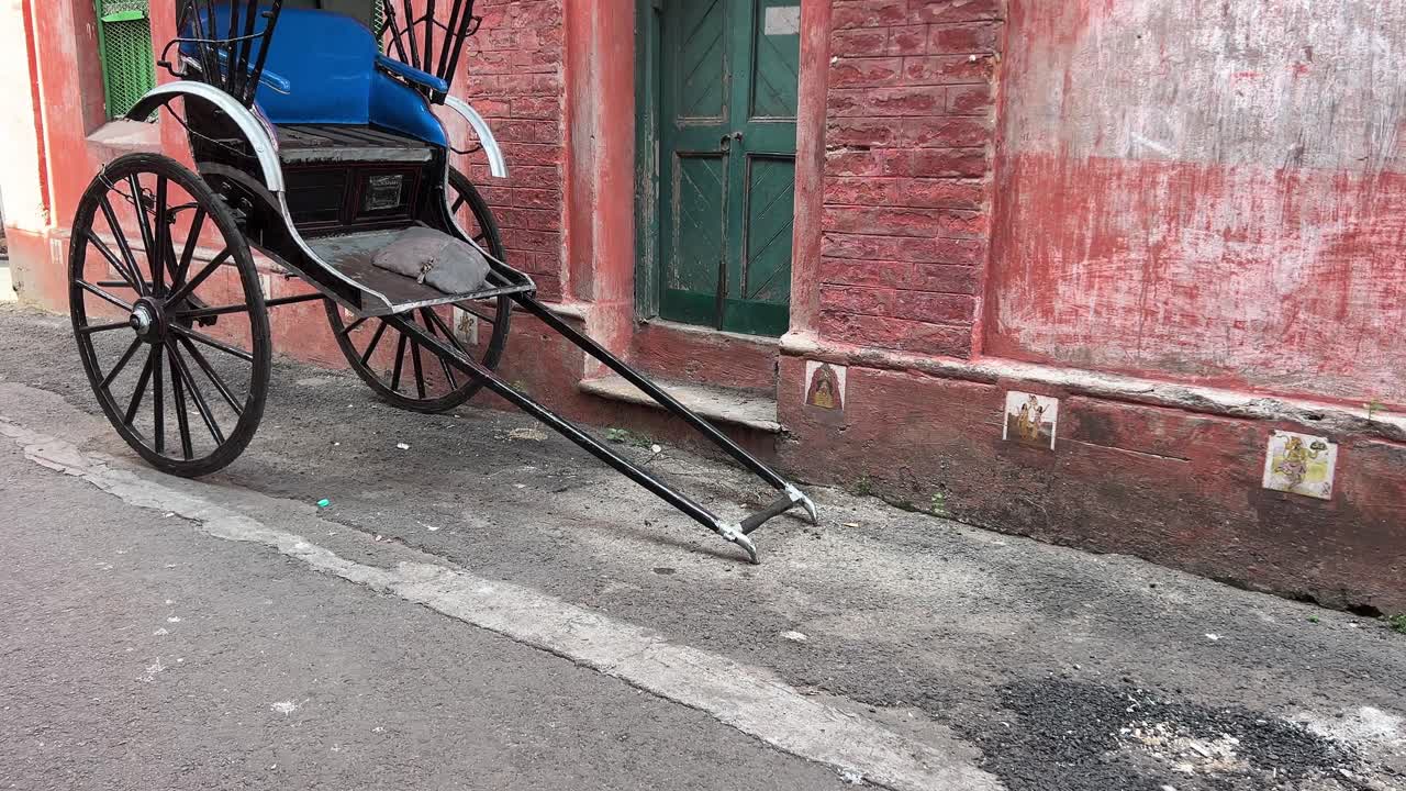 Profile view of hand pulled vintage rickshaw of Kolkata near a red color house with green vintage gate.