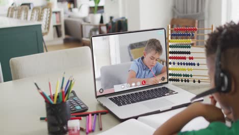 niño biracial en la computadora portátil aprendiendo en línea con un escolar caucásico