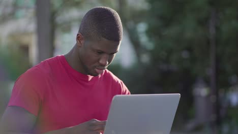 young afro-american muscular man working on laptop in park