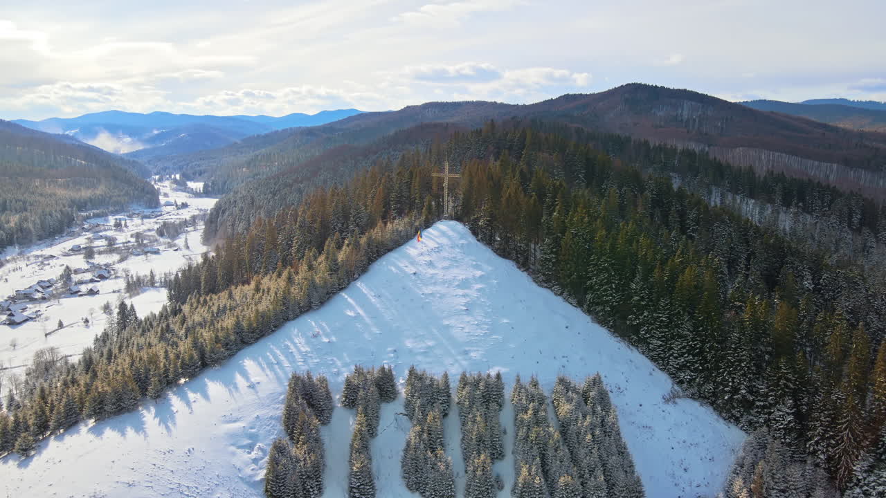 Letecký dronový pohled na nápis Stefan na kopci v Putně v zimě, Rumunsko. Holé stromy, sníh, kopec s křížem na vrcholu.