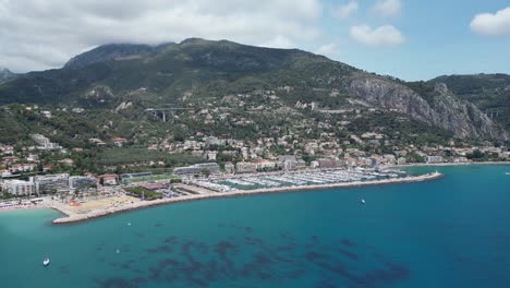 Approaching-boat-marina-at-beach-town-of-Menton-in-Southern-France,-Aerial-dolly-in-shot