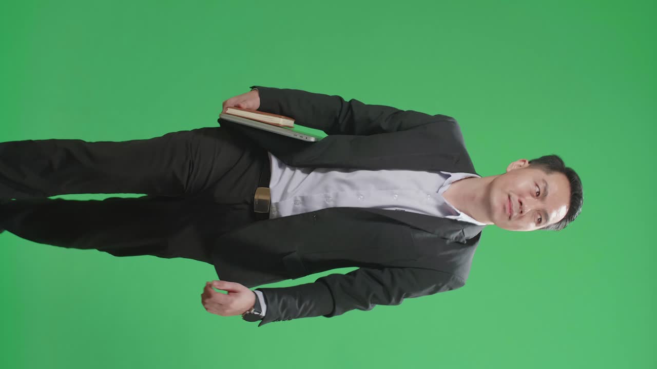 Asian Business Man Holding Book And Laptop While Walking On Green Screen Chroma Key