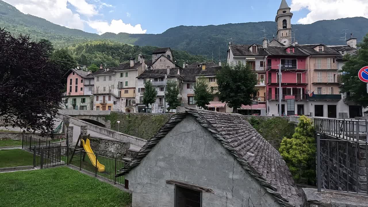 Colorful buildings and stone rooftops in the alpine town of Varzo, with a church bell tower and mountain backdrop in Piedmont, Italy