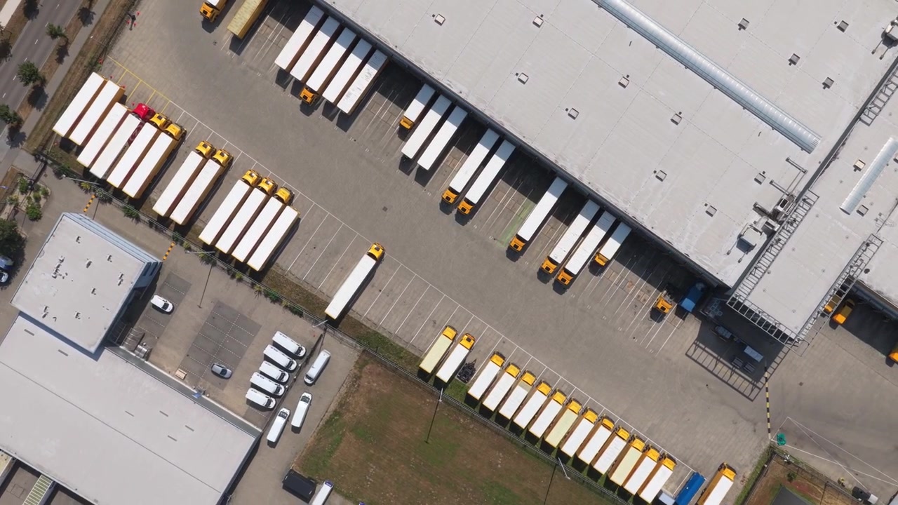 Fugleperspektiv af adskillige leveringslastbiler og sættevogne parkeret ved et stort lagerdistributionscenter, klar til lastning og forsendelse