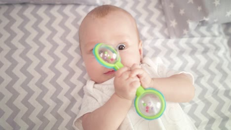 Portrait of cute baby boy playing toy. Cute child playing with rattle on bed